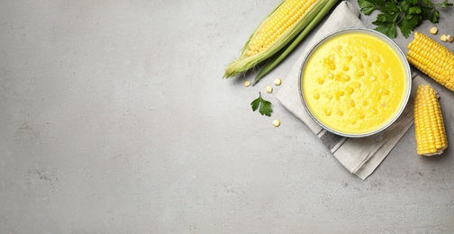Photo of Delicious creamy corn soup and cobs on grey table, flat lay. Space for text