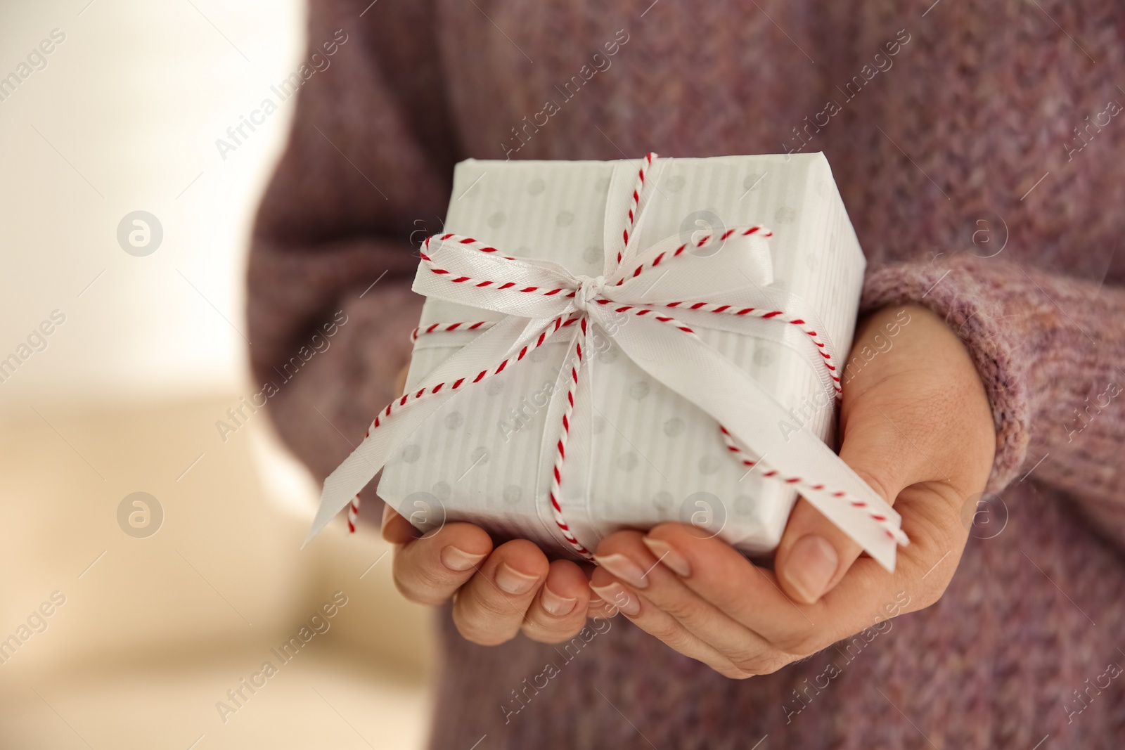 Photo of Woman holding white Christmas gift box indoors, closeup