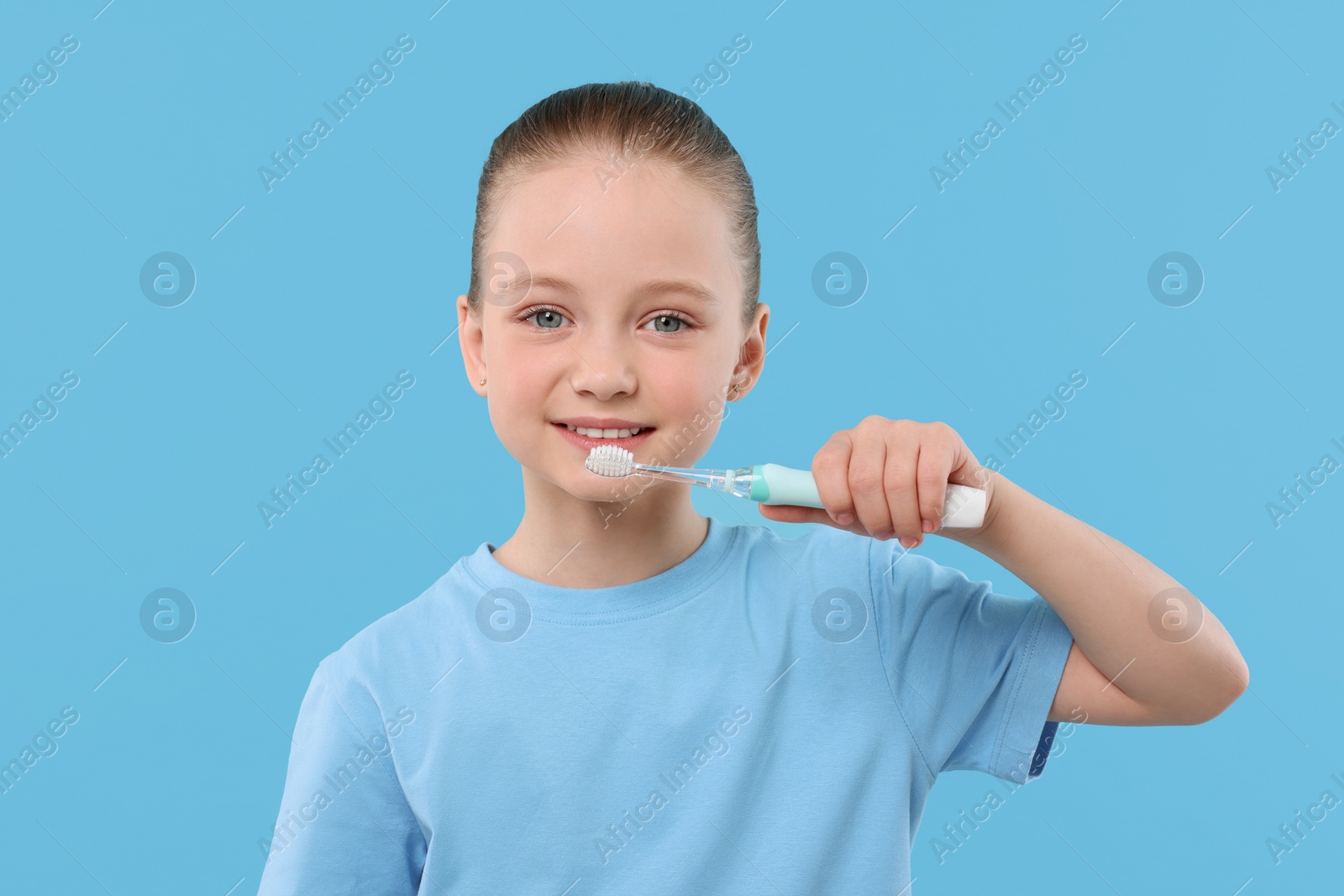 Photo of Happy girl brushing her teeth with electric toothbrush on light blue background