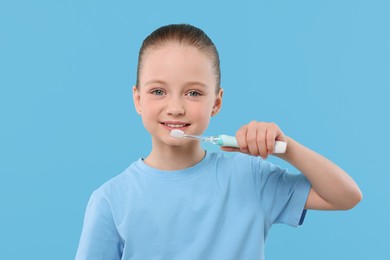 Photo of Happy girl brushing her teeth with electric toothbrush on light blue background