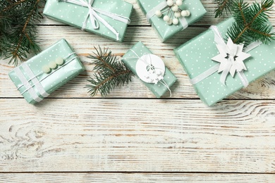 Photo of Christmas gift boxes with fir branches on white wooden background, flat lay. Space for text