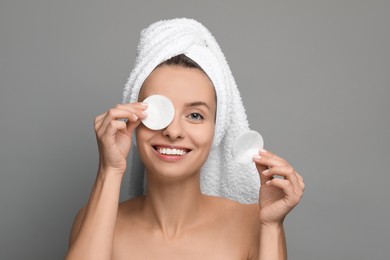 Photo of Smiling woman removing makeup with cotton pads on grey background