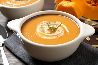 Photo of Tasty creamy pumpkin soup with dill and seeds in bowl on table