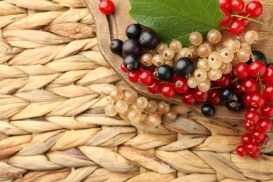 Photo of Different fresh ripe currants and green leaf on wicker surface, flat lay. Space for text