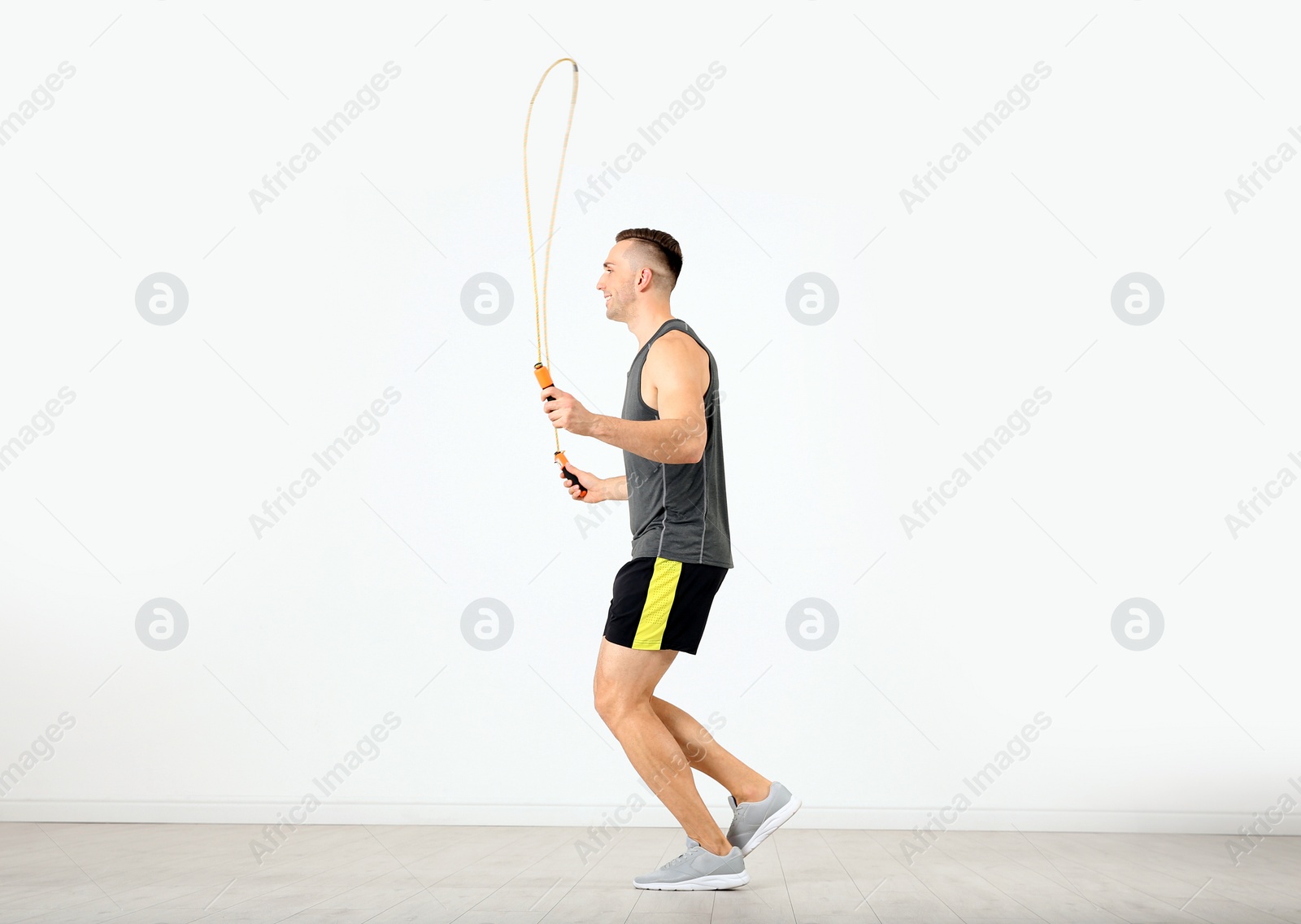 Photo of Young sportive man training with jump rope in light room