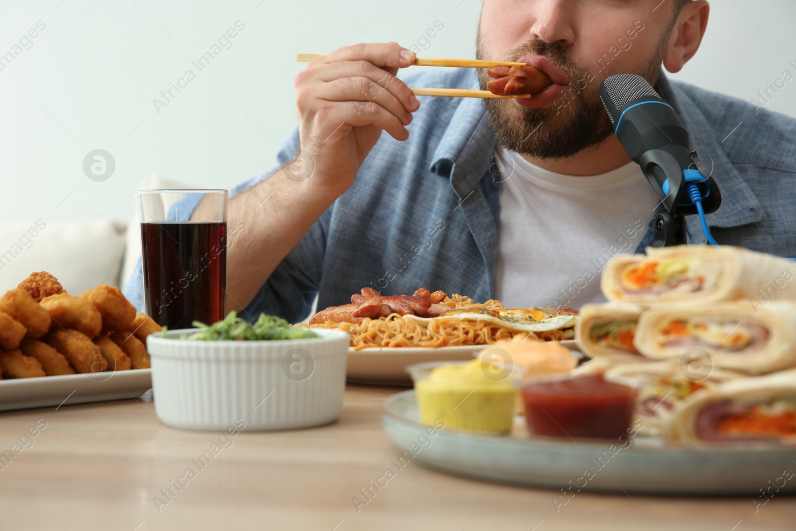 Photo of Food blogger eating in front of microphone at table against light background, closeup. Mukbang vlog