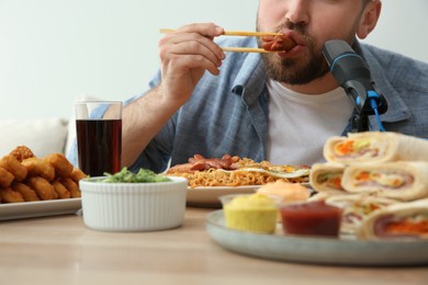 Photo of Food blogger eating in front of microphone at table against light background, closeup. Mukbang vlog