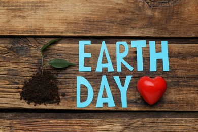 Photo of Words Earth Day, soil with plant and decorative heart on wooden table, flat lay