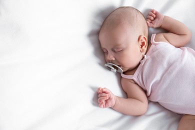 Photo of Cute little baby with pacifier sleeping on bed, top view. Space for text
