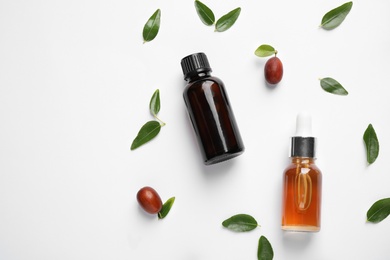 Photo of Glass bottles with jojoba oil and seeds on white background, top view