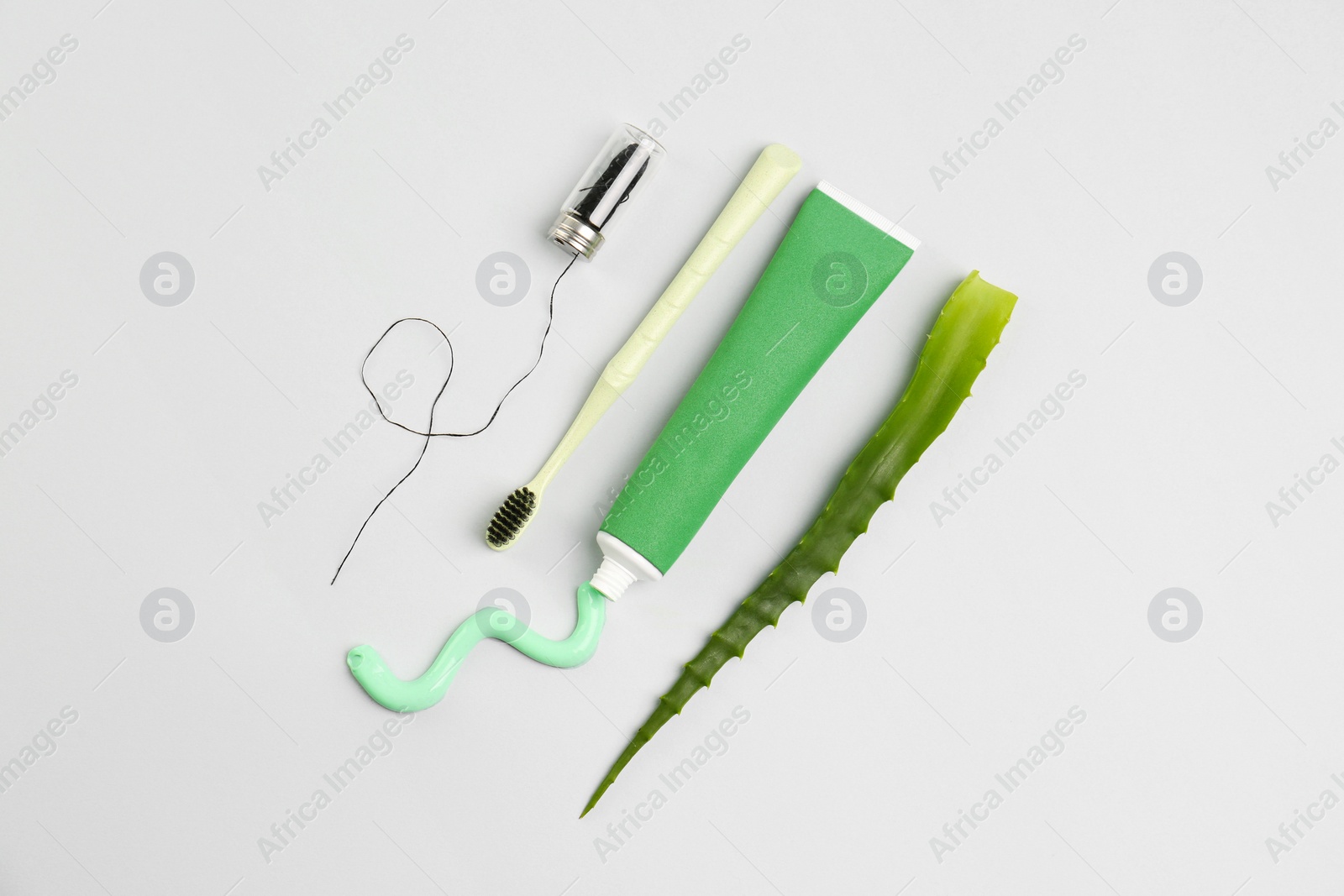 Photo of Tube of toothpaste, toothbrush, dental floss and fresh aloe on light grey background, flat lay