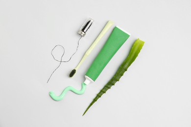 Photo of Tube of toothpaste, toothbrush, dental floss and fresh aloe on light grey background, flat lay