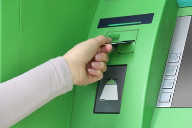 Woman inserting credit card into green cash machine, closeup