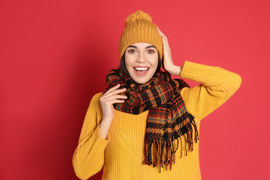 Photo of Young woman wearing warm sweater, scarf and hat on red background. Winter season