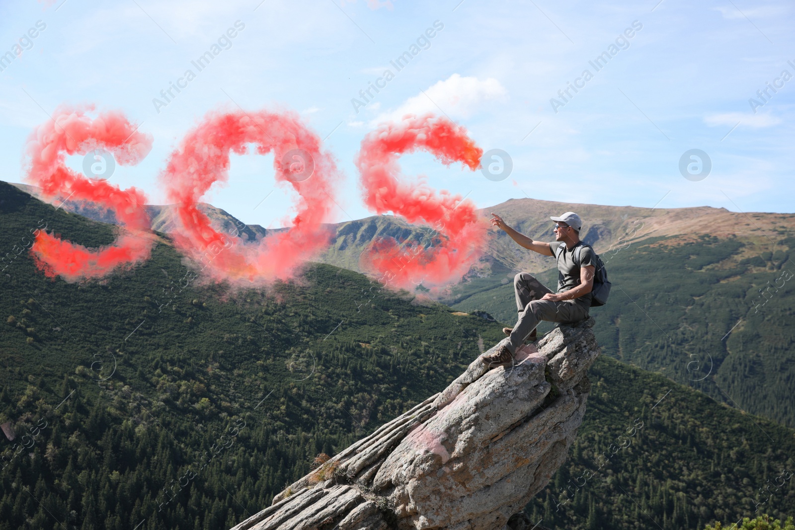 Image of Man with backpack and word SOS made of color smoke bomb on rocky peak in mountains