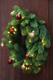 Beautiful Christmas wreath with baubles and string lights hanging on brown wooden wall