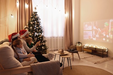 Photo of Family watching Christmas movie via video projector in cosy room. Winter holidays atmosphere