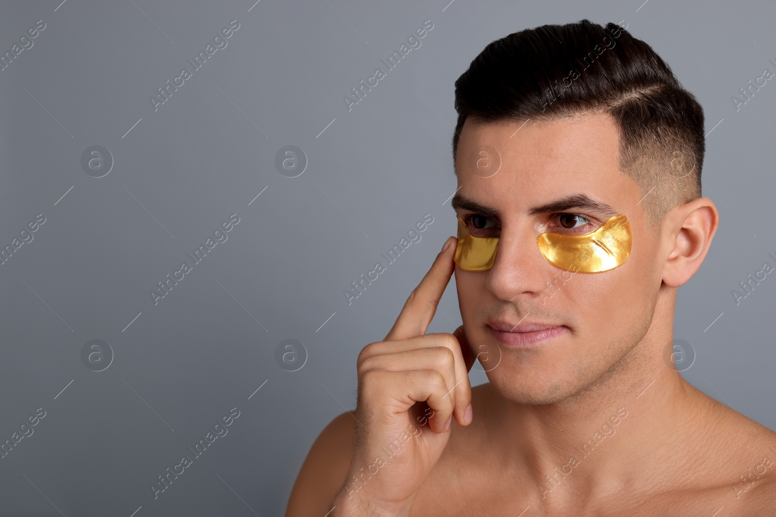 Photo of Man applying golden under eye patch on grey background. Space for text