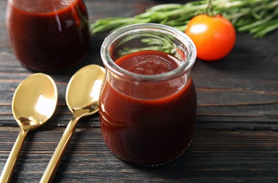 Photo of Glass jar of barbecue sauce and spoons on wooden table