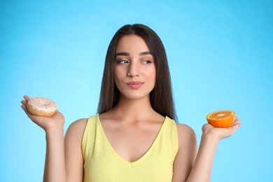 Photo of Woman choosing between orange and doughnut on light blue background