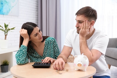 Unhappy young couple with piggy bank and money at home. Financial problems