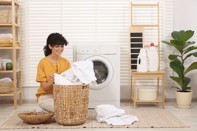 Happy woman with laundry near washing machine indoors
