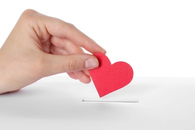 Woman putting red heart into slot of donation box against white background, closeup