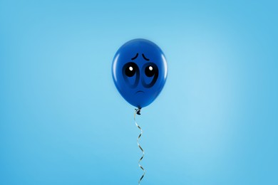 Blue balloon with sad face on light blue background