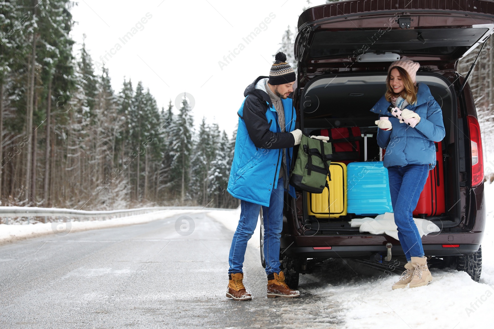 Photo of Couple near open car trunk full of luggage on road, space for text. Winter vacation