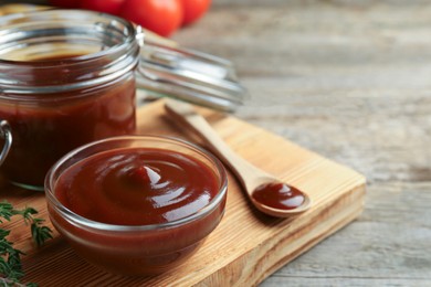 Photo of Tasty barbeque sauce in bowl, jar and spoon on wooden table, closeup. Space for text