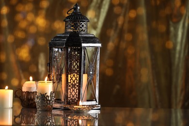 Photo of Arabic lantern and burning candles on mirror surface against blurred lights, space for text