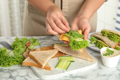 Photo of Woman making tasty sandwich at white marble table, closeup