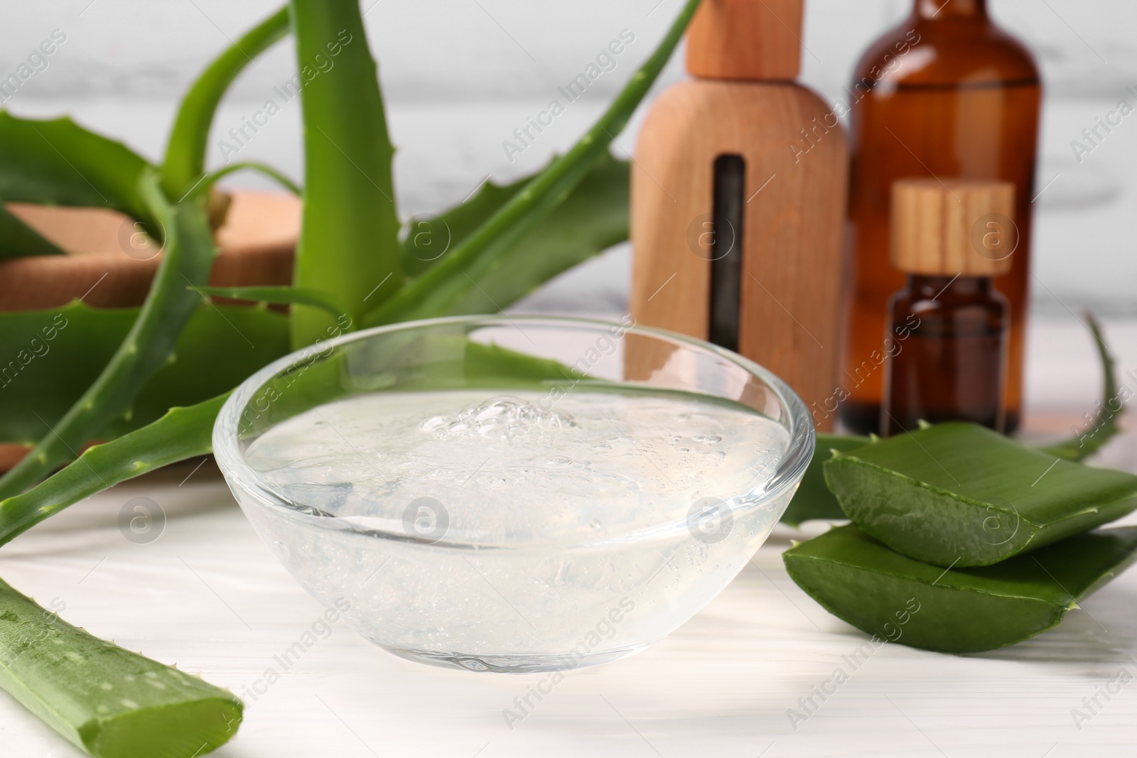 Photo of Bowl of cosmetic gel and cut aloe vera leaves on white wooden table, closeup