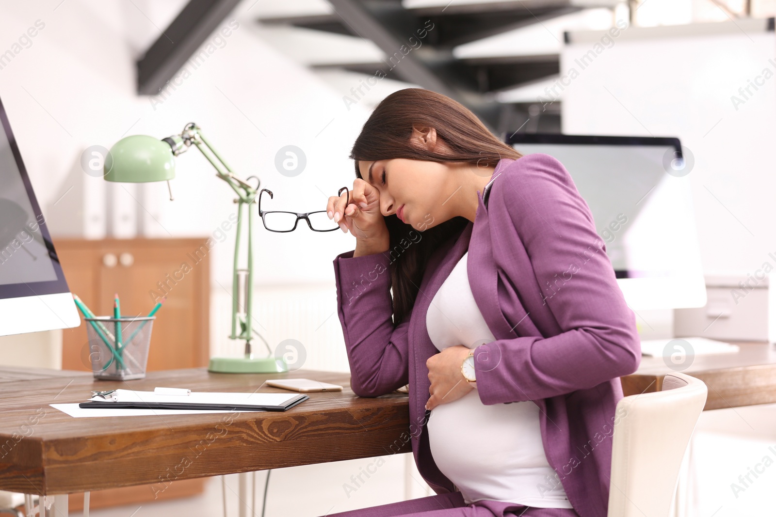 Photo of Young pregnant woman suffering from pain while working in office