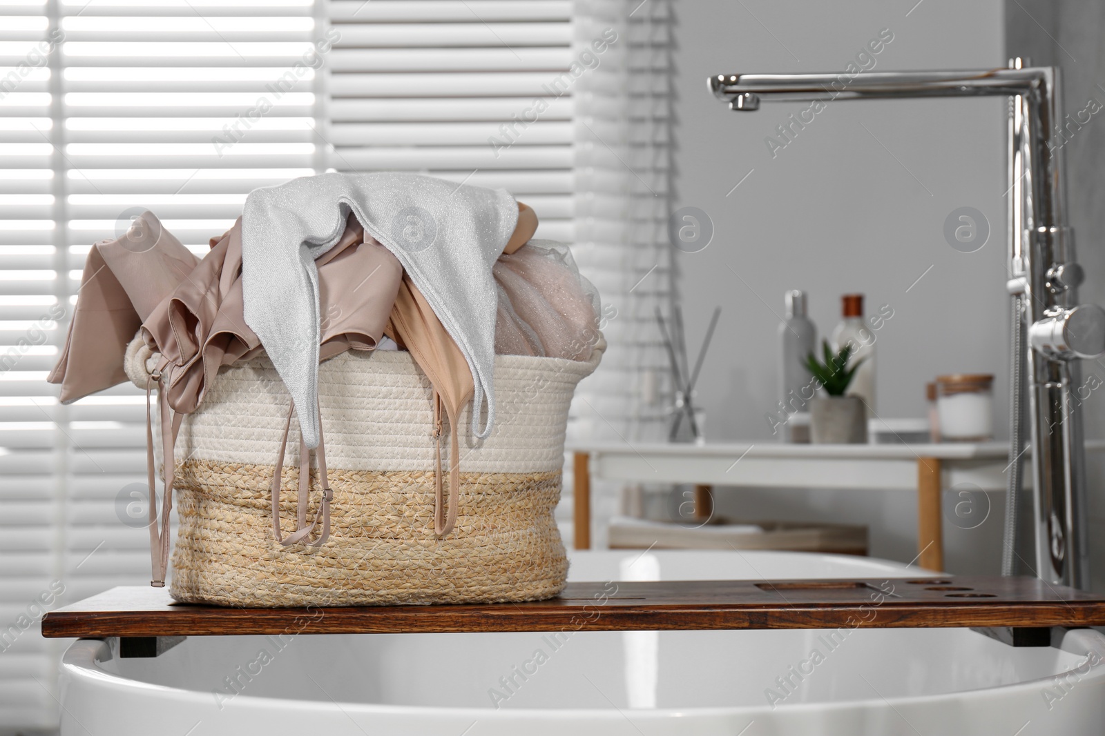 Photo of Wicker laundry basket with clothes on wooden tray in bathroom