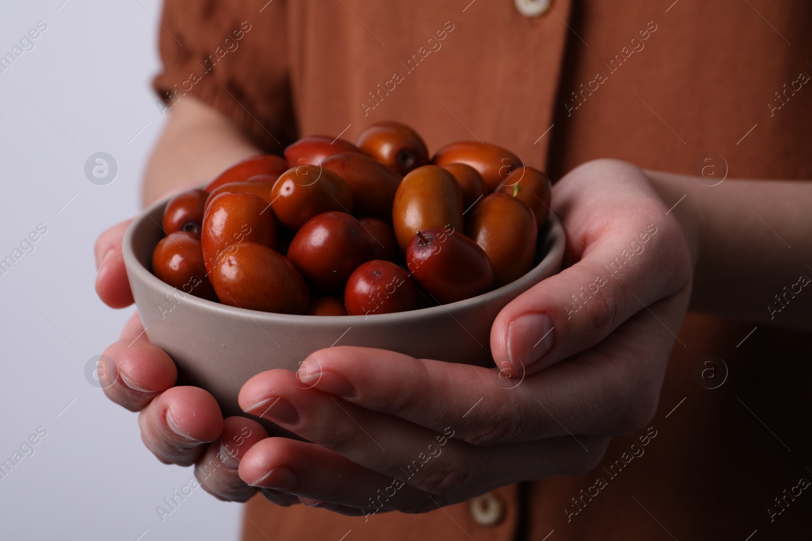 Photo of Woman holding bowl with fresh Ziziphus jujuba fruits on light background, closeup