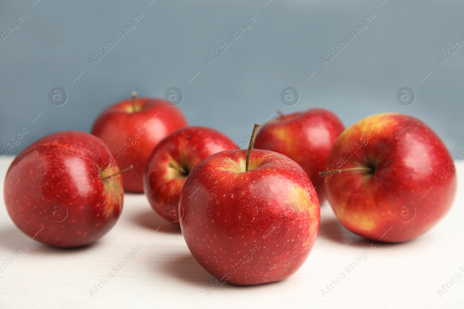 Photo of Ripe juicy red apples on white wooden table against blue background. Space for text