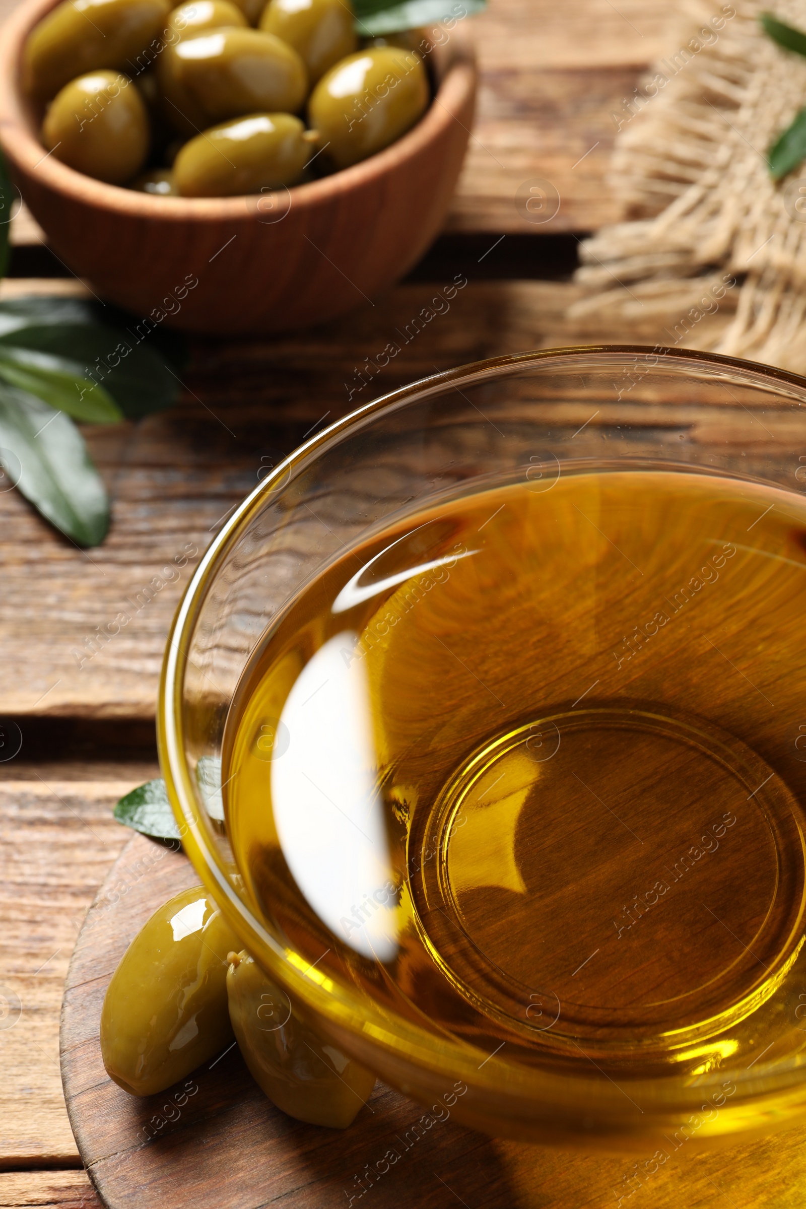 Photo of Glass bowl of oil and ripe olives on wooden table, closeup