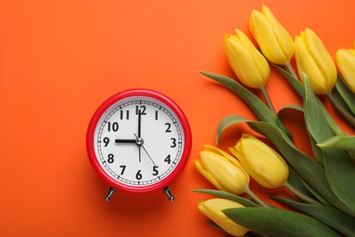 Red alarm clock and beautiful tulips on orange background, flat lay. Spring time