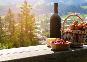 Bottle of red wine and food for picnic on bench against mountain landscape