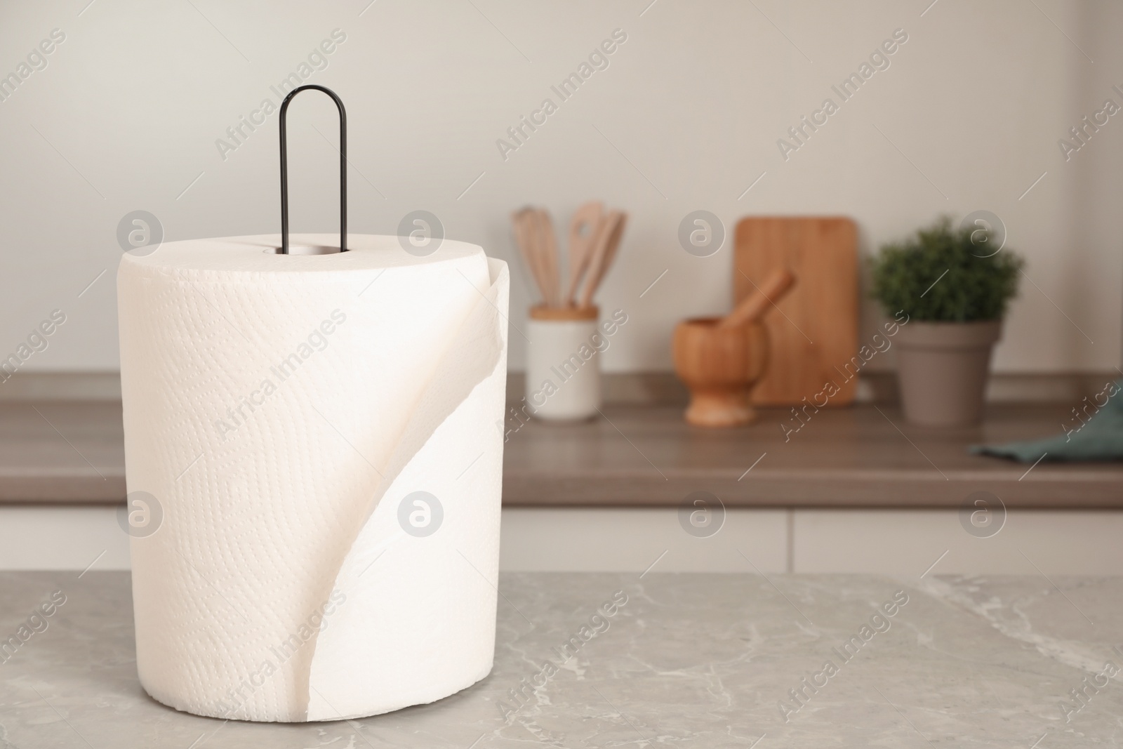 Photo of Holder with roll of white paper towels on light grey marble table in kitchen. Space for text