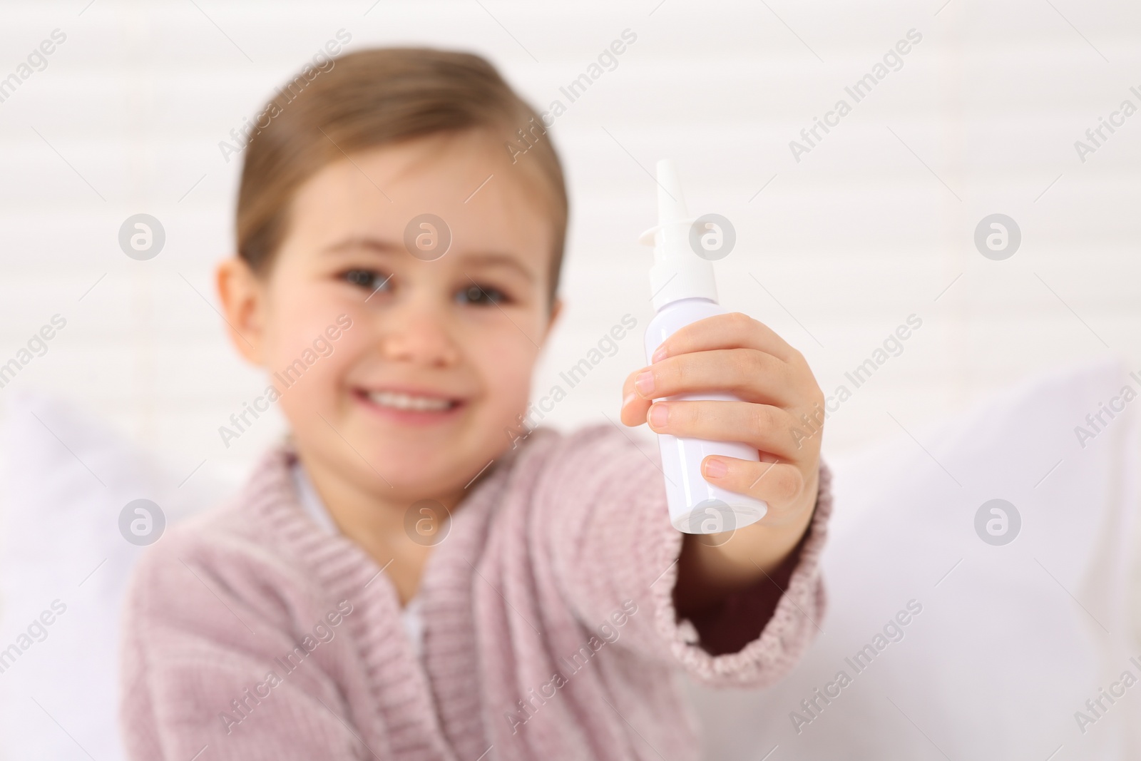 Photo of Cute little girl showing nasal spray indoors, focus on hand