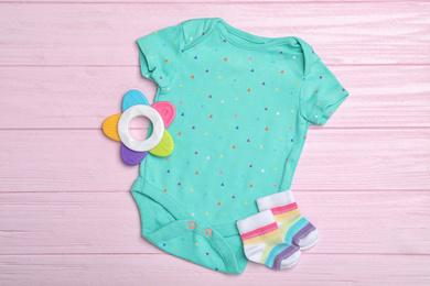 Child's clothes and teether on pink wooden background, flat lay