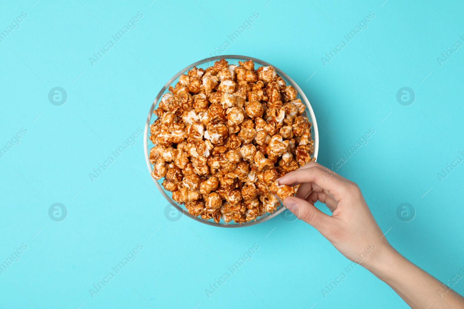 Photo of Woman eating tasty popcorn from bowl on color background, top view