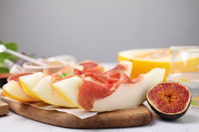 Photo of Tasty melon, jamon and figs served on white tiled table, space for text