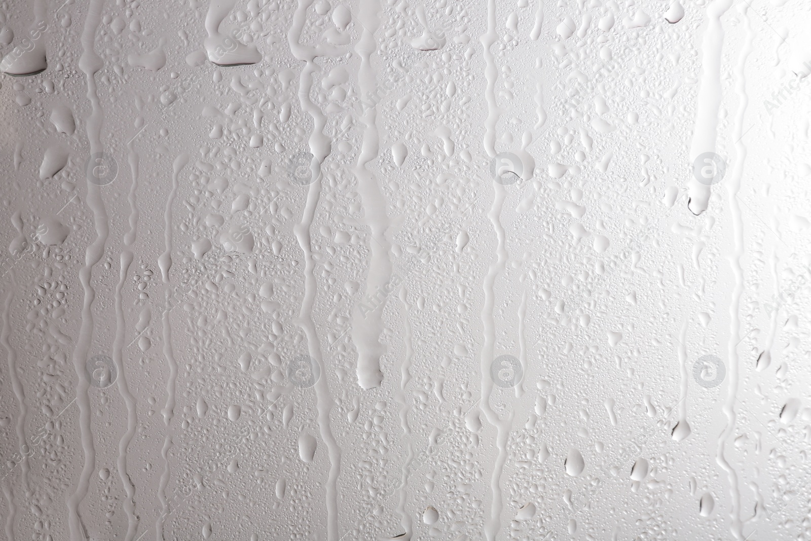 Photo of Glass with rain drops against light background