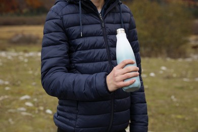 Photo of Boy holding thermo bottle with drink in mountains, closeup