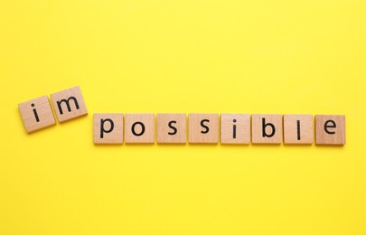 Photo of Motivation concept. Changing word from Impossible into Possible by removing squares with letters I and M on yellow background, top view
