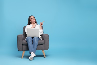 Photo of Smiling young woman with laptop sitting in armchair on light blue background, space for text