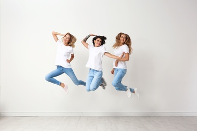 Photo of Group of young women in jeans jumping near light wall